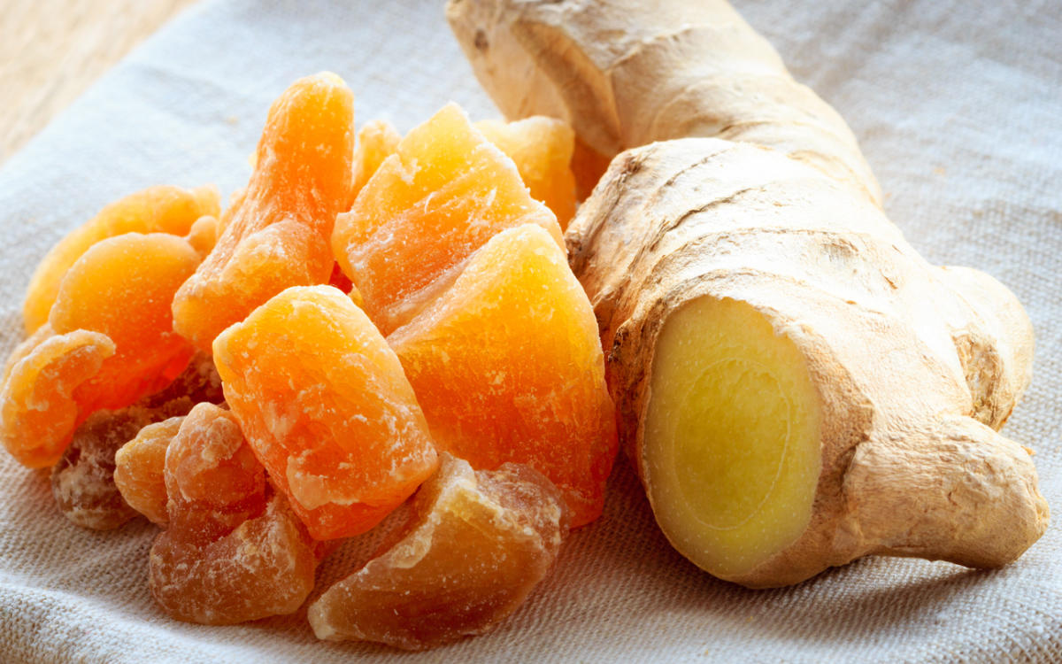 Closeup dried candied crystallized ginger pieces and fresh rhizome root on rustic table. Healthy eating, home remedy for nausea, colds.