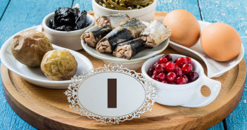 Products containing iodine (seaweed, boiled eggs, cranberries, sardines, baked potatoes, prunes) on a round cutting board and a blue wooden background