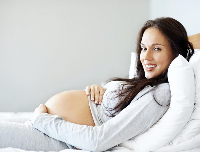 Portrait of a happy young pregnant lady lying comfortably on the bed
