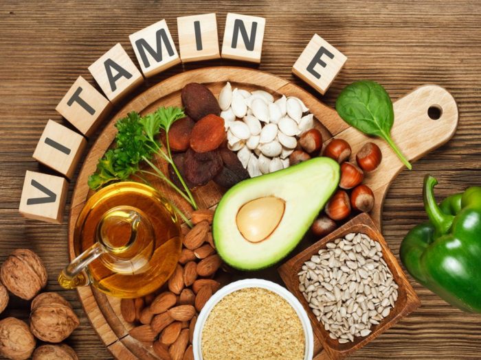 Foods rich in vitamin E such as wheat germ oil, dried wheat germ, dried apricots, hazelnuts, almonds, parsley leaves, avocado, walnuts, pumpkin seeds, sunflower seeds, spinach and green paprika on wooden table