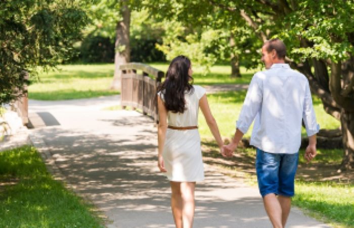 Влюбленная пара гуляет в летнем парке, держась за руки.