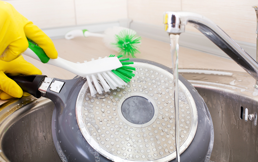 Close up of female hands with rubber gloves cleaning frying pan with brush in the kitchen