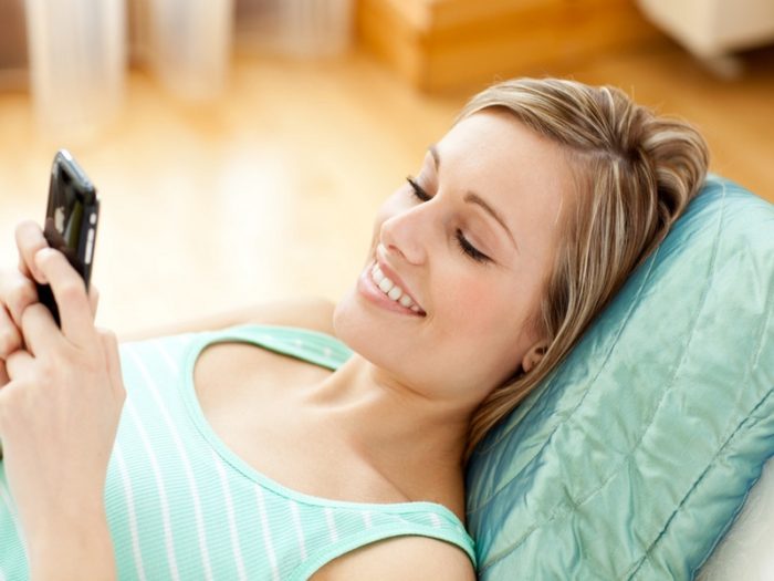 Jolly young woman sending a text lying on a sofa