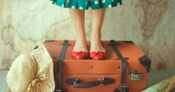 woman-in-polka-dot-dress-standing-on-suitcase-with-map-in-background