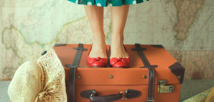 woman-in-polka-dot-dress-standing-on-suitcase-with-map-in-background