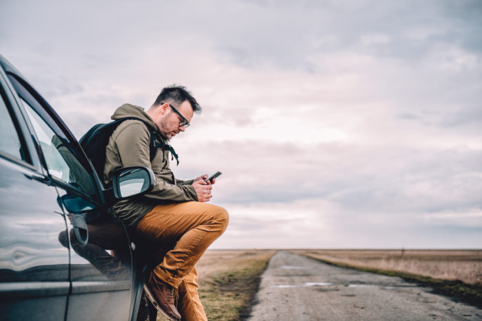 Man sitting on the car and using smart phone