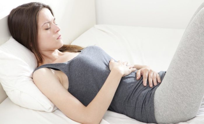 Young woman holding her stomach in pain lying on a bed.