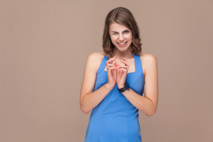 Playfully woman in blue dress looking at camera with sly look. Indoor shot