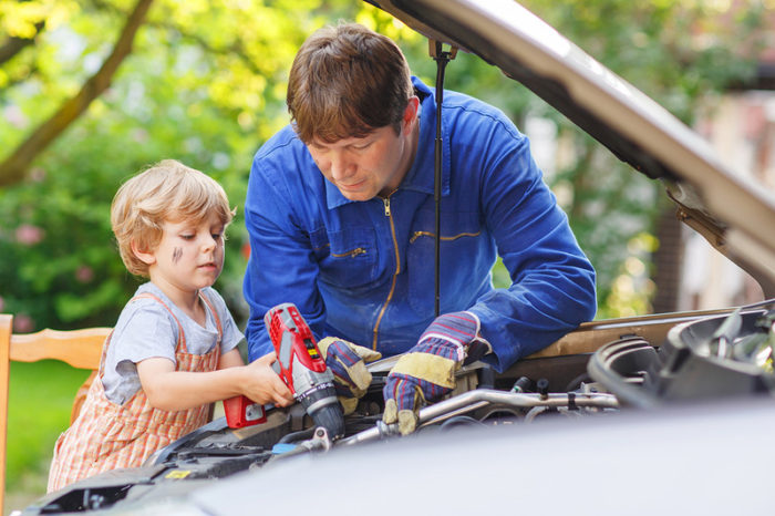 Young father teaching his little boy to repair motor oil in family car.