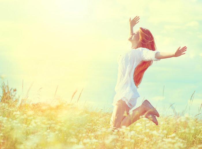 Beauty model girl in white dress jumping on summer field