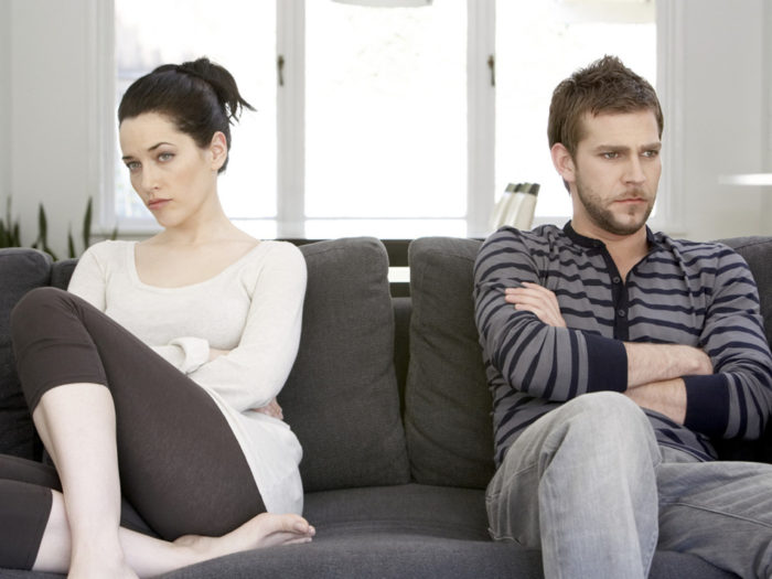 Couple sitting on sofa with arms folded, looking angry