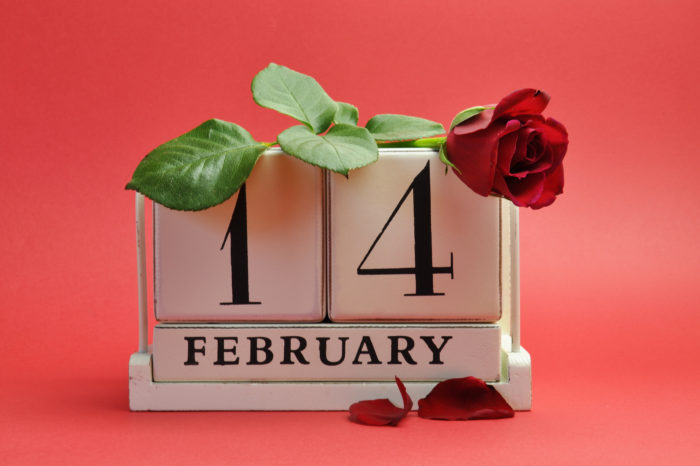 Mark the date white wooden calendar, St Valentine Day February 14, with a red rose against a red background.