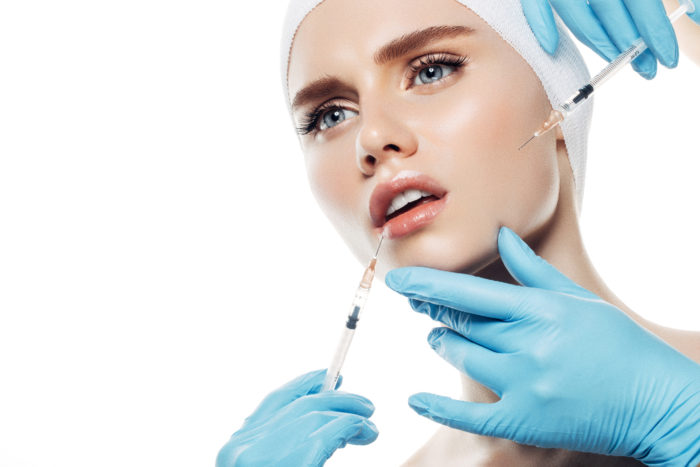 Studio shot of young beautiful woman having facial injections on white background. Professional make-up