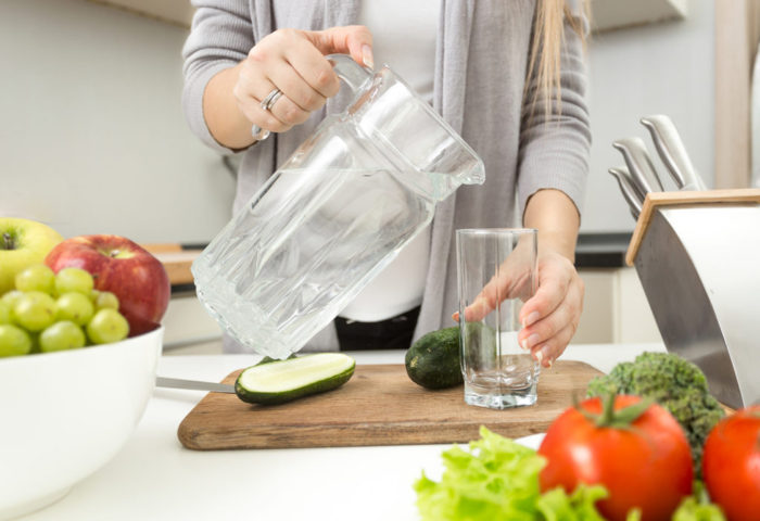 Closeup photo of woman pouring water in glass on kitchen