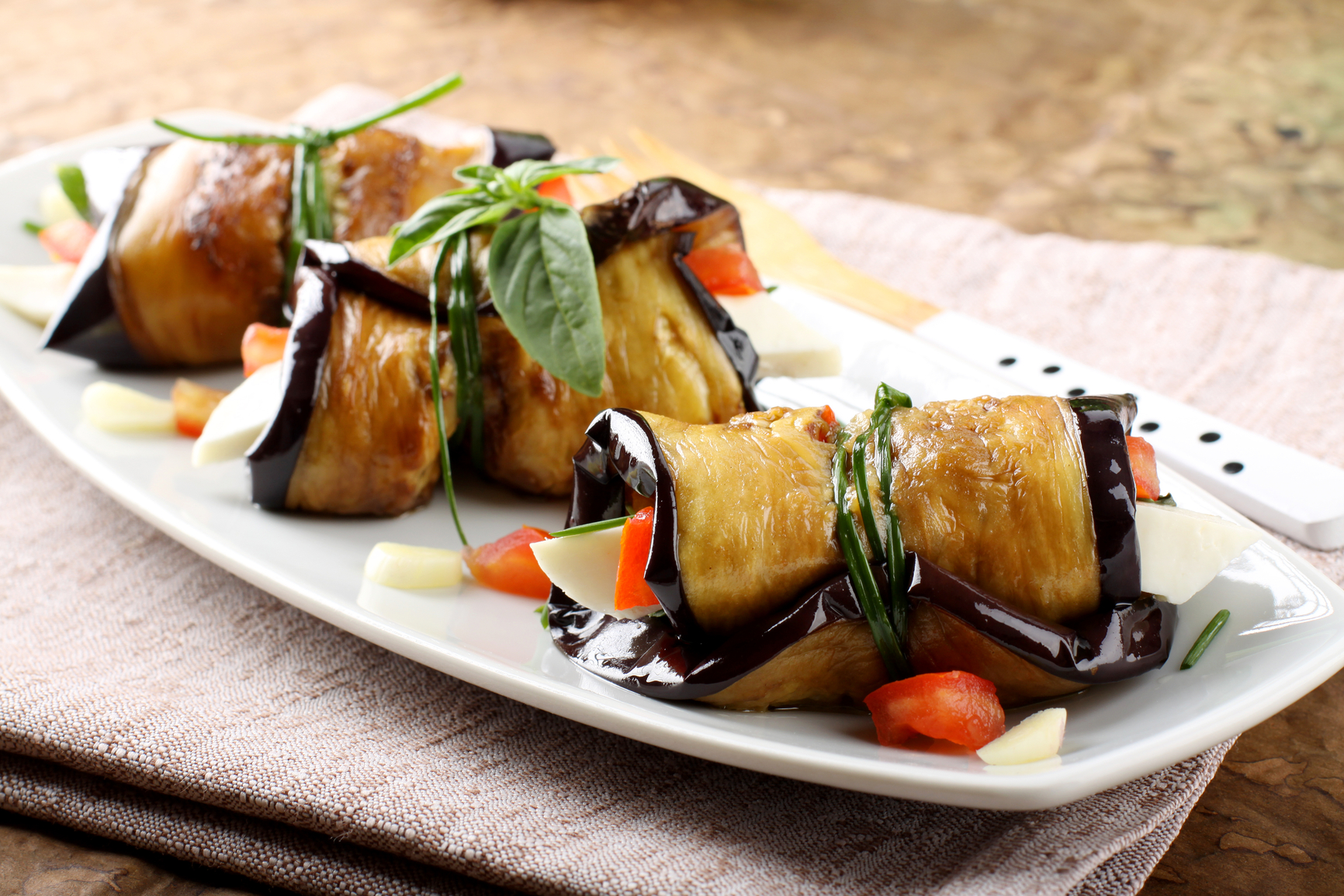 Eggplant rolls with cheese, tomato and basil on complex background