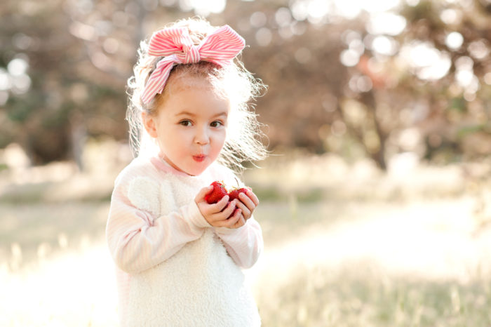 Cute kid girl holding strawberries outdoors. Looking at camera.