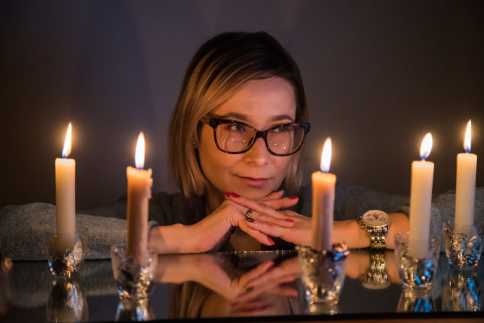 Romantic girl in the glass sitting near a table with candles in a dark room