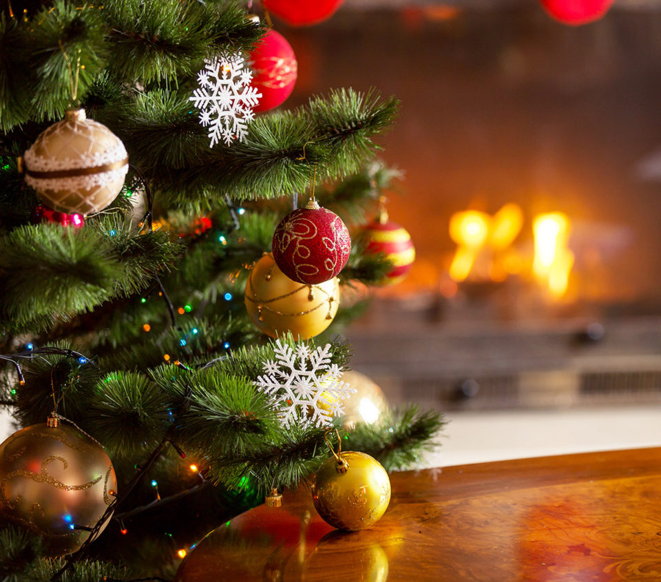 Closeup image of golden and red baubles on Christmas tree in front of burning fireplace. Beautiful Christmas background