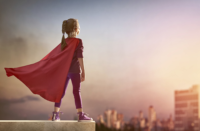 Little child girl plays superhero. Child on the background of sunset sky. Girl power concept
