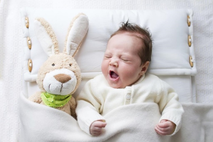Yawning newborn baby near toy rabbit