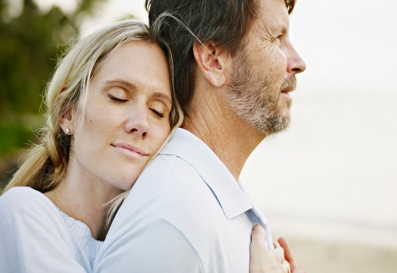 Wife embracing husband on beach at sunset